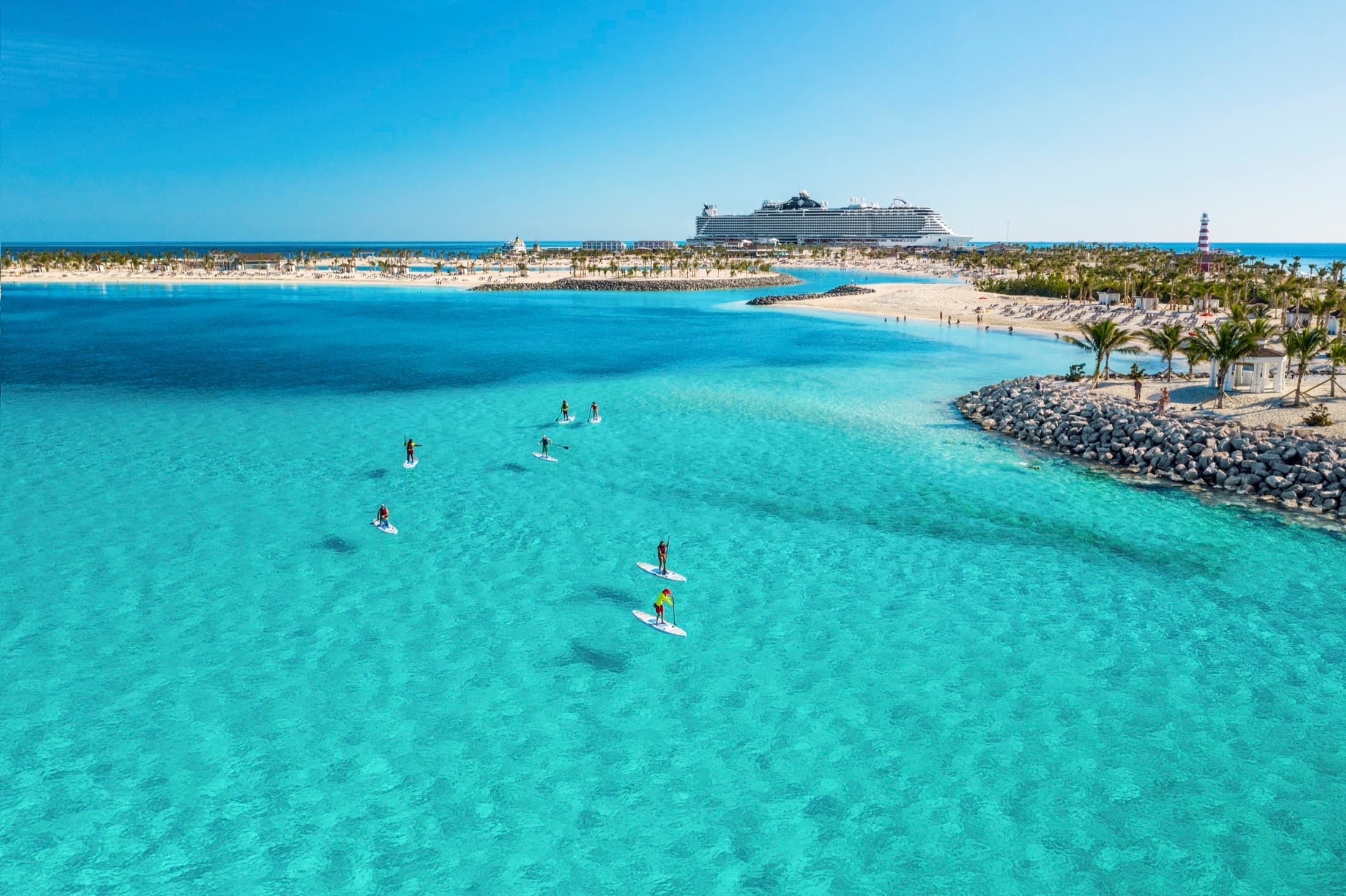 Paddleboarders in a turquoise lagoon at Ocean Cay, with a cruise ship on the horizon